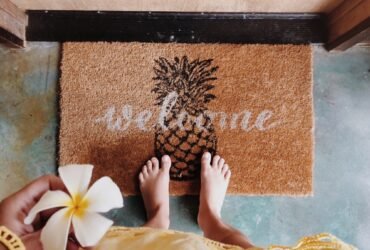 Woman standing on the door mat with a welcome writing holding frangipani flower in her hand